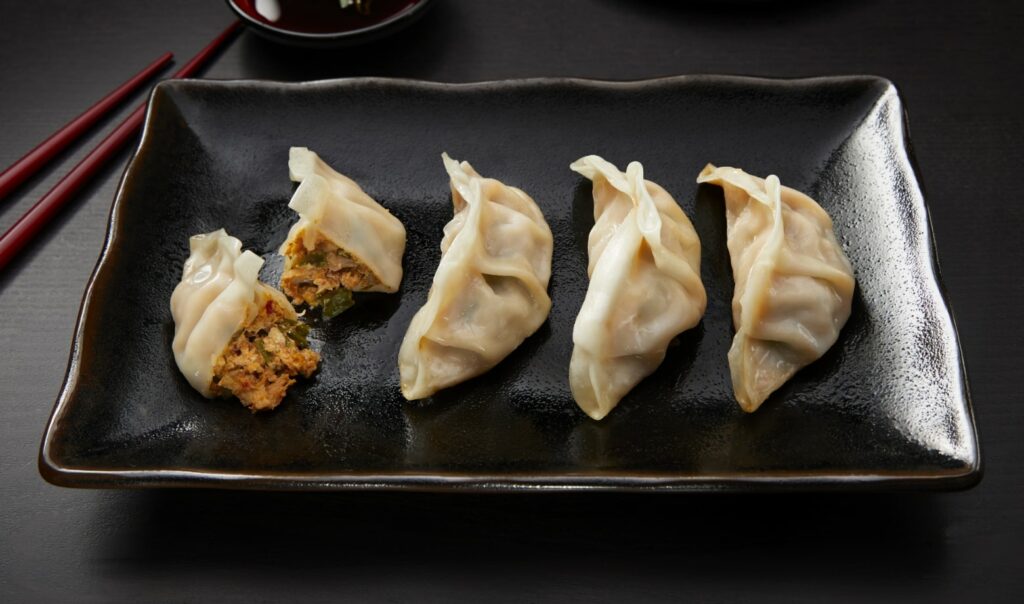 four dumplings on a serving tray, one is sliced in half to show the filling inside
