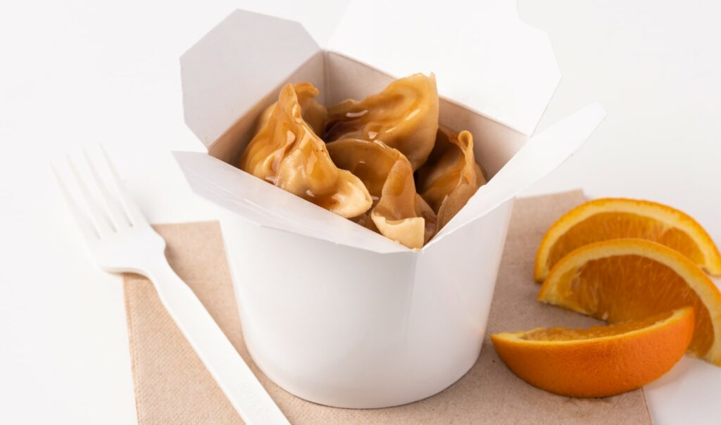 a takeout container filled with dumplings next to some orange slices