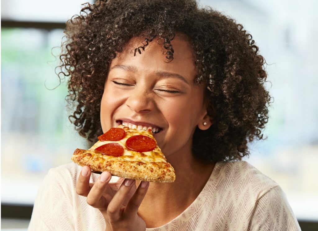 young woman smiling while she enjoys eating a slice of pizza