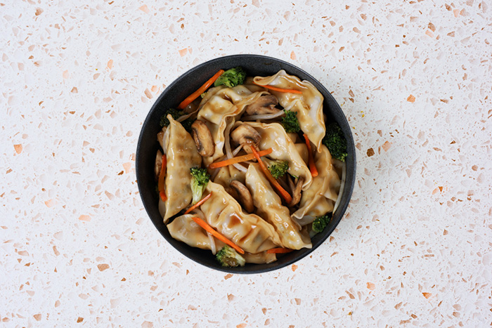 Potsticker stir fry in a black bowl with broccoli and carrots on light colored terrazzo tabletop