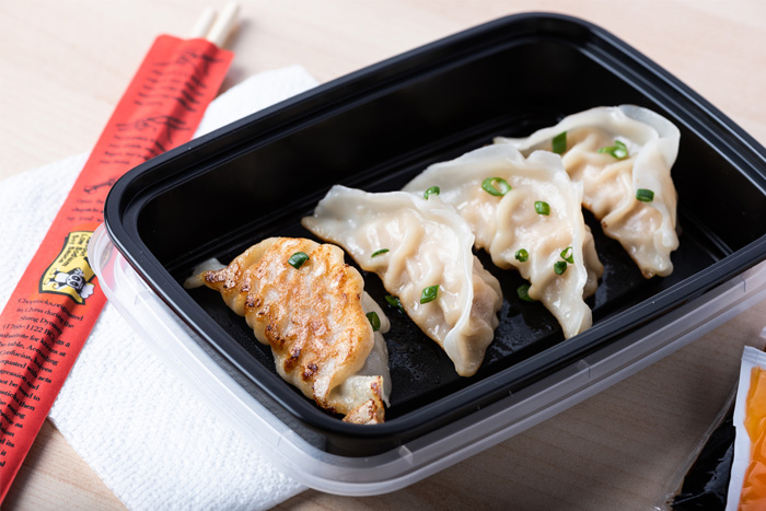 four pan fried dumplings in take out box with disposable chopsticks and sauce packets on the side