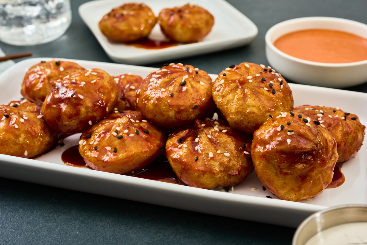 Pile of fried dumplings coated in gochujang, white and black sesame seeds resting on a white serving plate. 