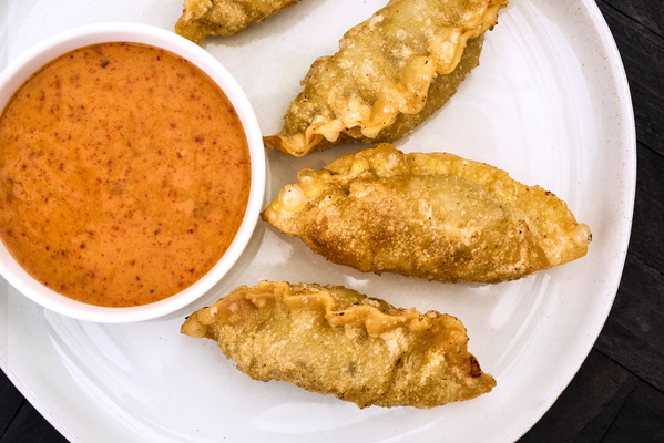 four deep fried Chef One Beef Dumplings with a side of gochujang mayo on a white plate.
