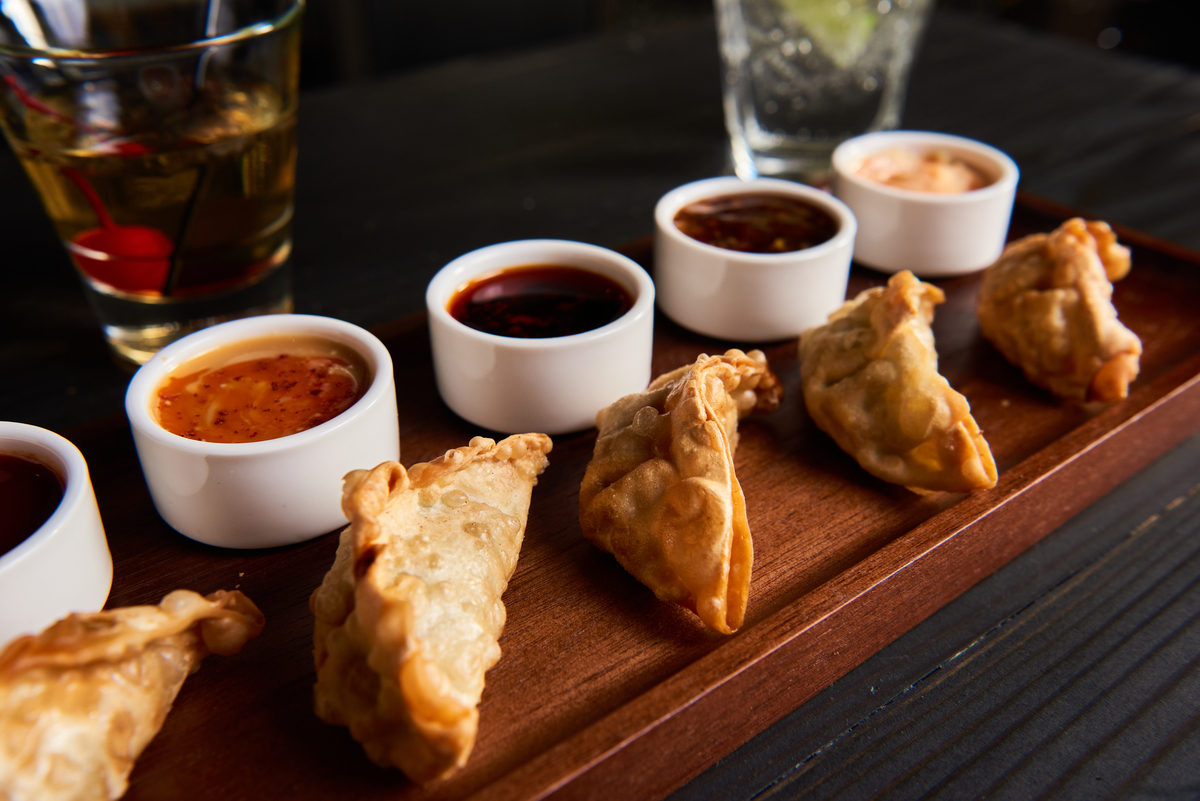 Fried dumplings on a charcuterie board with four ramekins containing different sauce flavors including sweet and spicy, teriyaki and gochujang. 