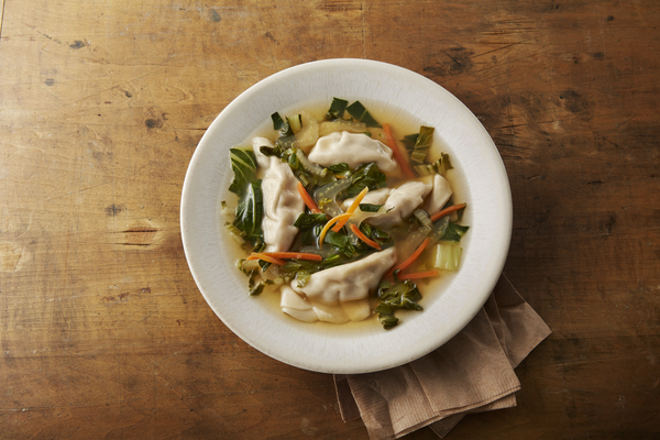 Soup with four dumplings, bok choy and carrots in a clear, golden broth.
