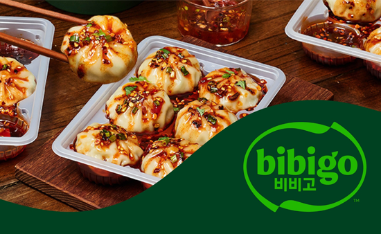 bibigo dumpling tray with six dumplings covered in a spicy soy sauce.
