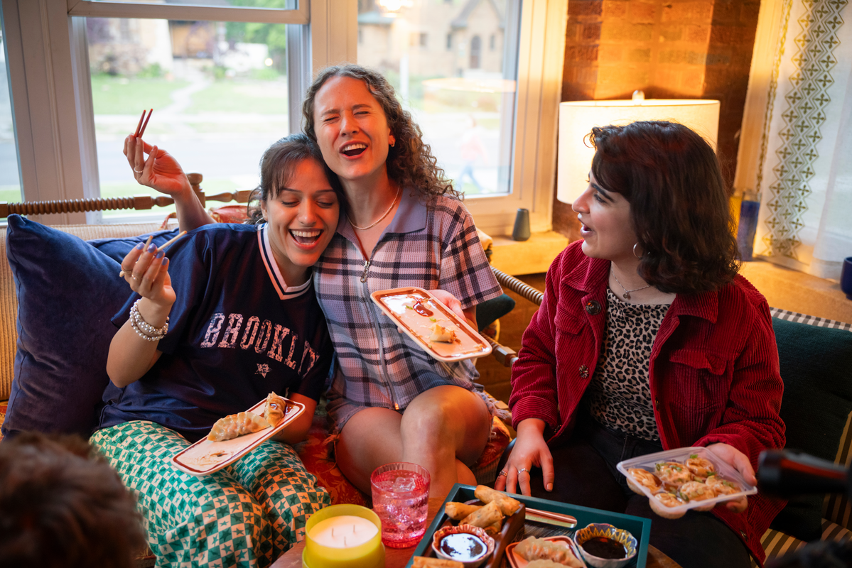Three young women smiling and enjoying bibigo™ steamed dumplings together at a table.