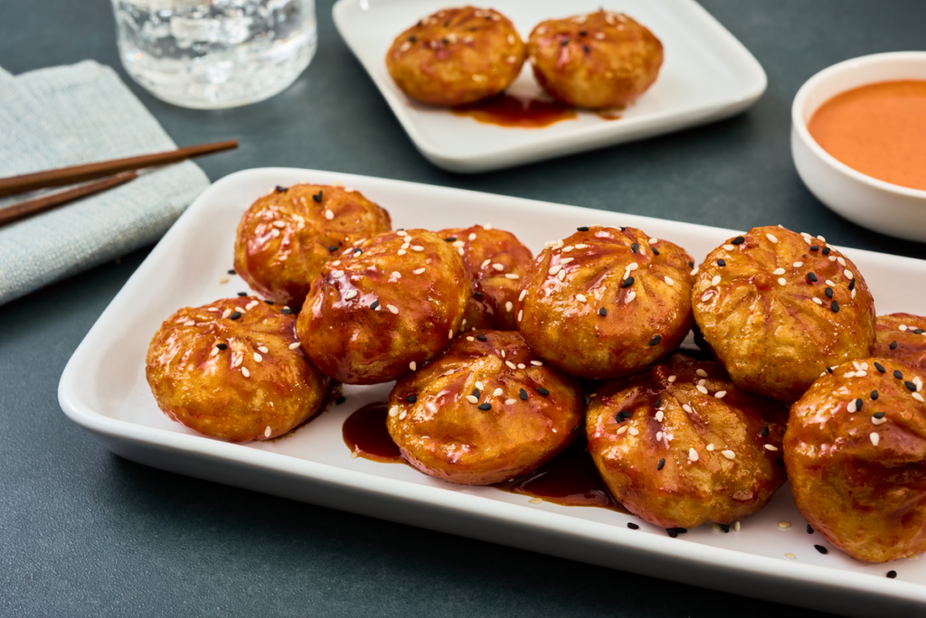 Plated fried chicken and vegetable dumplings drizzled with sweet and spicy gochujang sauce on a serving platter.