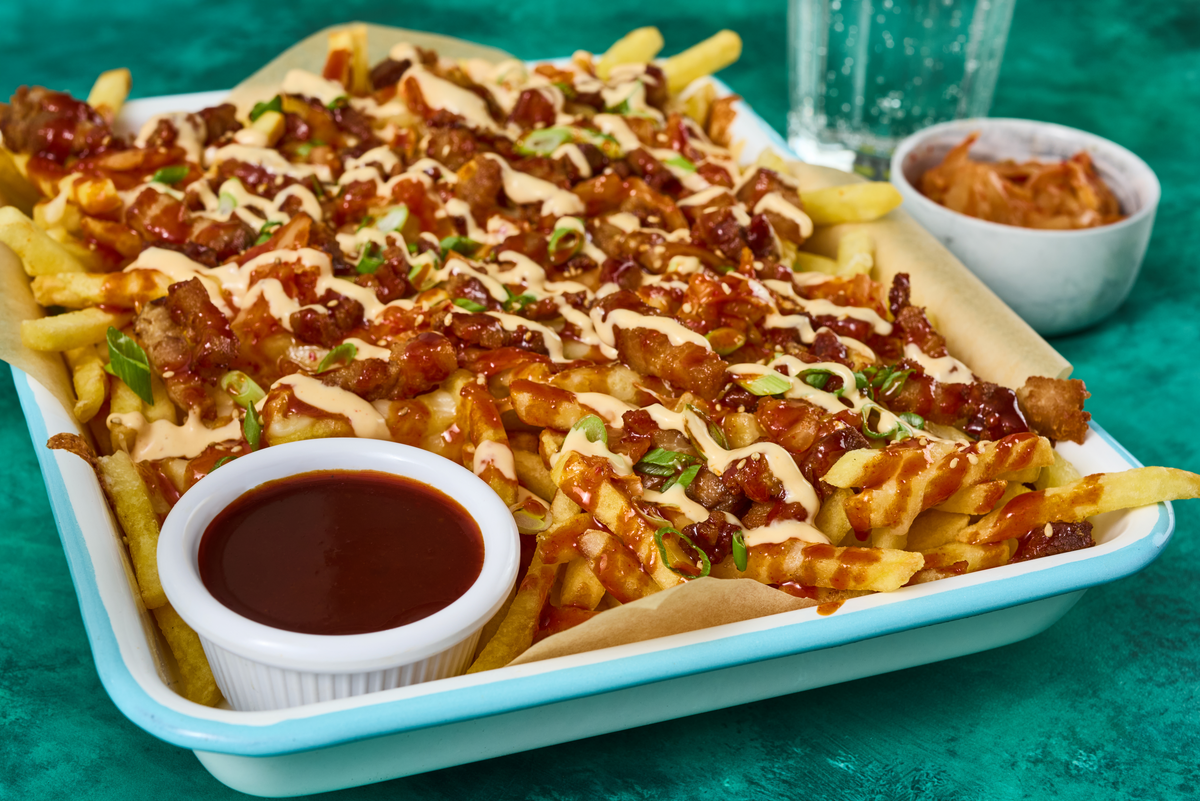 Alt Text: A platter of loaded french fries topped with sauce, green onions, and cheese, served with a small side bowl of dipping sauce.