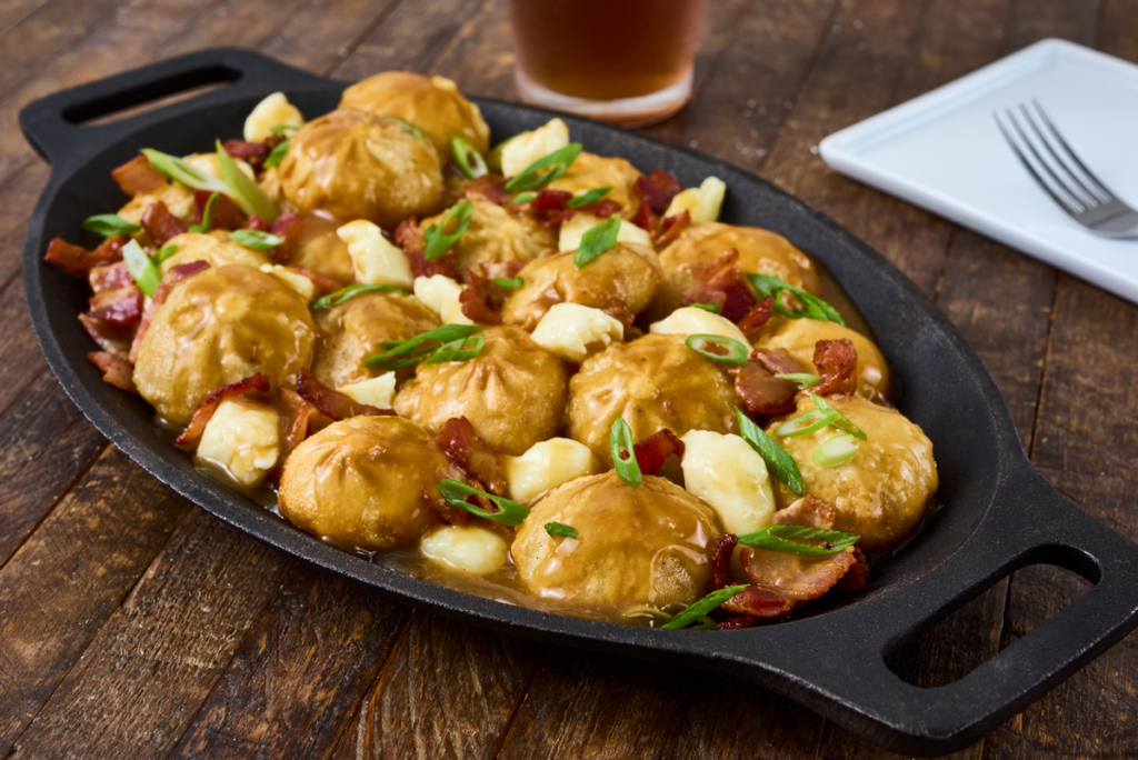 A dish of bibigo™ steamed dumpling poutine topped with gravy, cheese curds, and sliced green onions.