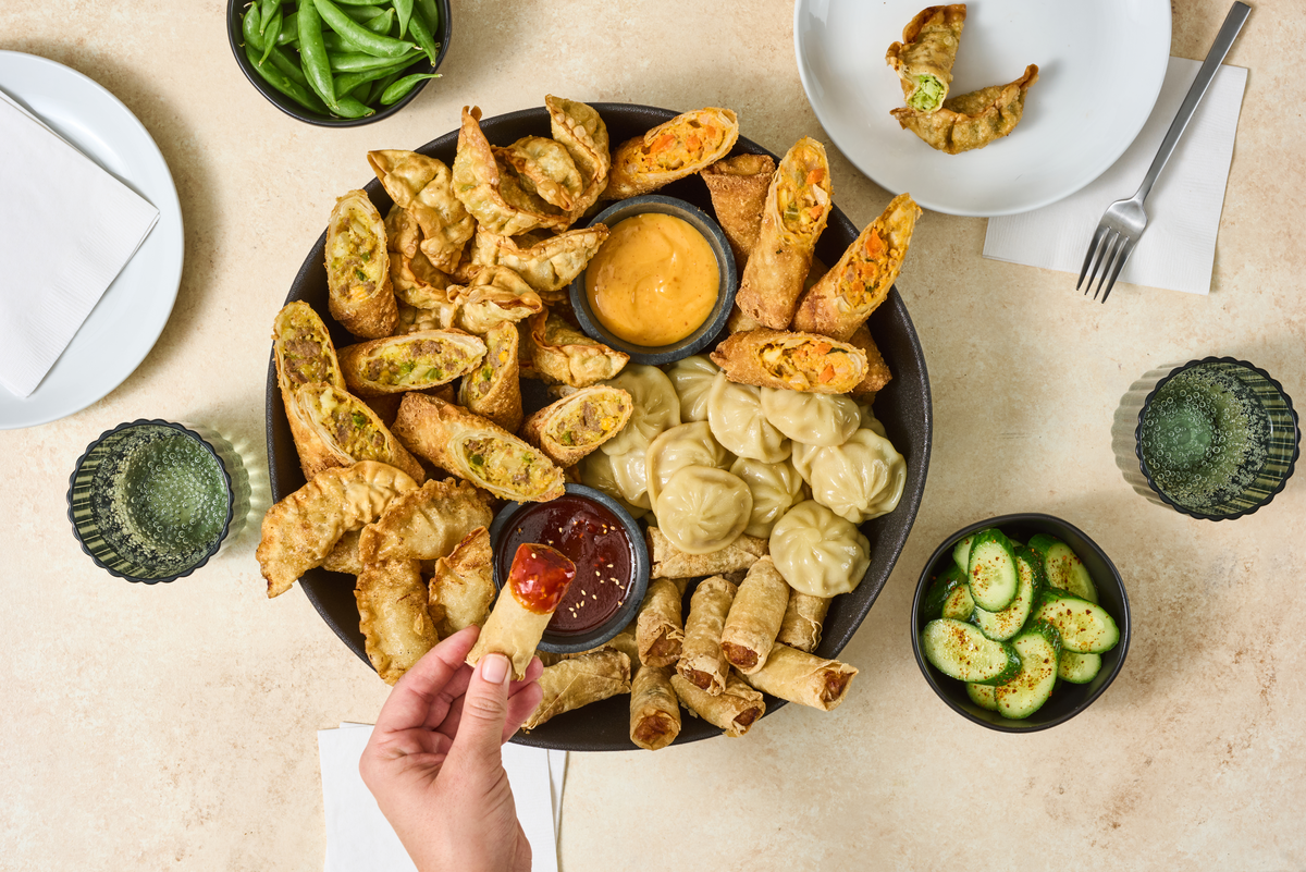 An assortment of Asian appetizers—including egg rolls, dumplings, and wontons—arranged on a large serving platter with dipping sauces.