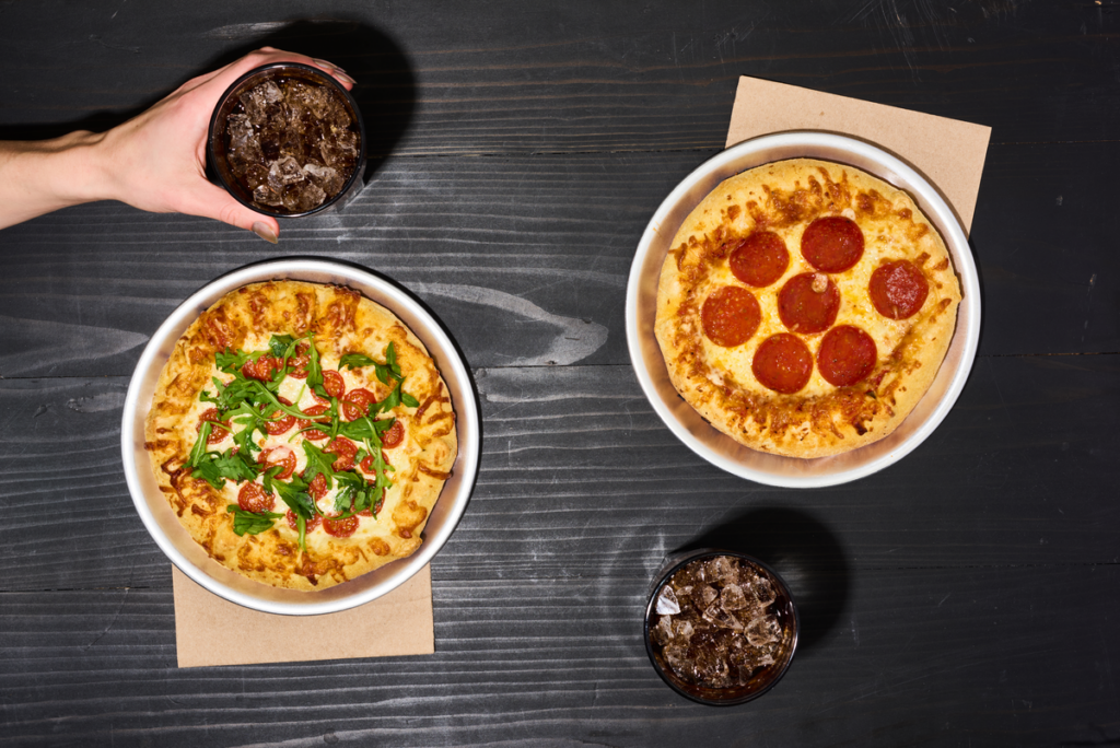 Two VILLA PRIMA® personal pizzas topped with cheese, basil, tomatoes, and pepperoni on a dark tabletop.